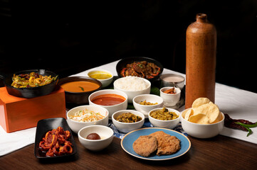 Goan fish thali with rawa fried kingfish, crab, calamari, prawns, fish curry, rice, papad, dal, thrissur, sol curry, gulab jamun, served in bowls and plate with copper water bottle on brown table