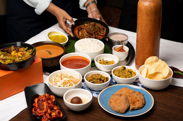 Goan fish thali with rawa fried kingfish, crab, calamari, prawns, fish curry, sambar, rice, papad, dal, thrissur, sol curry, gulab jamun, with hands placing crab plate in background on white cloth 