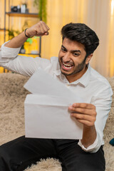 Indian man at home reading a letter with great news, celebrating a job offer, positive test...