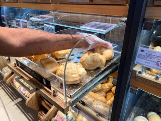 Conselve, Italy - May 16, 2025: Hand of a customer selecting fresh bread rolls from a display case...