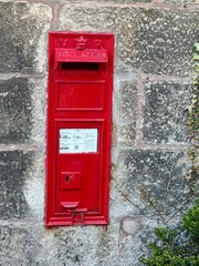 A traditional red Victorian-era post box set into a stone wall in the UK. The box is marked with...