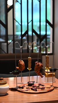 Display shot of two chicken tangdi kebabs and two mutton seekh kebabs on a barbecue curve kebab stand with dips, sauces, and a wooden platter, styled for a buffet.