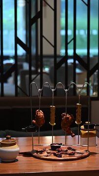 Display shot of two chicken tangdi kebabs and two mutton seekh kebabs on a barbecue curve kebab stand with dips, sauces, and a wooden platter, styled for a buffet.