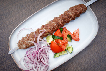 Grilled kebab with onions and tomatoes on a wooden table