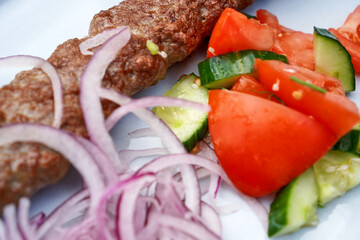 Close view of kebab with onions and vegetables on a plate
