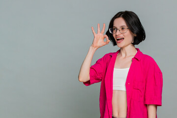 Young woman smiles and nods head confidently while forming an okay gesture with fingers, clearly...