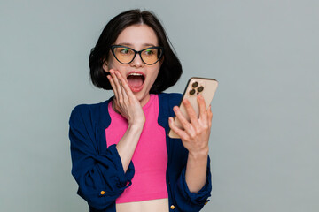 Young woman joyfully looks at smartphone screen in excitement celebrate winning an online game or...