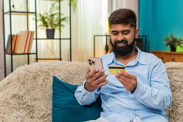 Indian man at home enters credit card on smartphone careful secure payment happy checkout process....