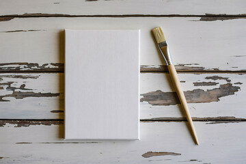 Blank white canvas with paintbrush on rustic wooden background