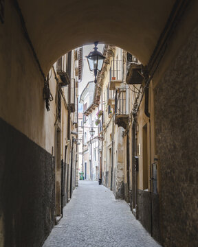 Fototapeta View of a long street beneath an archway with weathered walls and a hanging lantern casting soft light in Sulmona, Abruzzo, Italy.