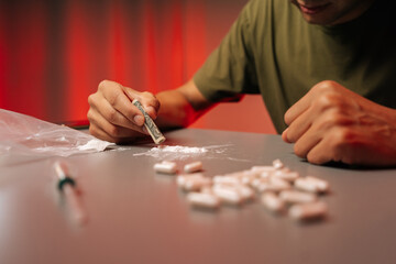 Close-up cropped shot of unrecognizable drug addict male arranging cocaine line near scattered pharmaceutical pills, revealing substance abuse risks on table. Concept of addiction and substance abuse.