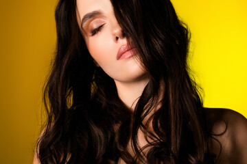 Charming young woman with brunette hair and glamorous makeup posing against yellow background