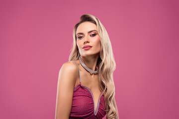Gorgeous blonde woman in an elegant dress with glamorous jewelry against a pink background