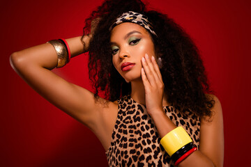 Glamorous young woman with bold makeup and leopard print top in stylish retro setting on red...