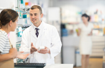 Polite male pharmacist speaking to woman customer buying medical preparation in large drugstore
