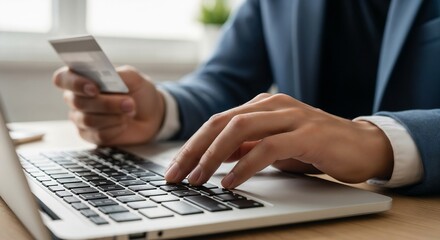 Fototapeta premium A man in a suit holding a credit card and typing on a laptop for online shopping.