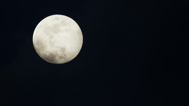 Full moon - super moon moves through the night sky behind of hazу of clouds.