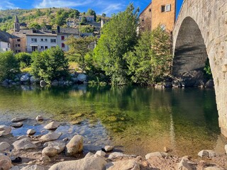 Lush green river flowing beneath a charming bridge in Pont-de-Montvert, Cévennes. Ideal for nature, landscape, and travel photography highlighting peaceful rural scenes.