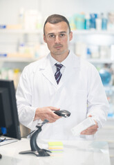 Young male pharmacist in uniform punches medicines at checkout counter in pharmacy