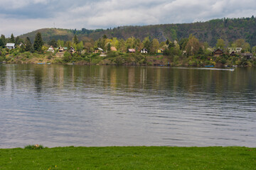 Peaceful riverside scene with green hills and scattered cottages reflected in calm water....