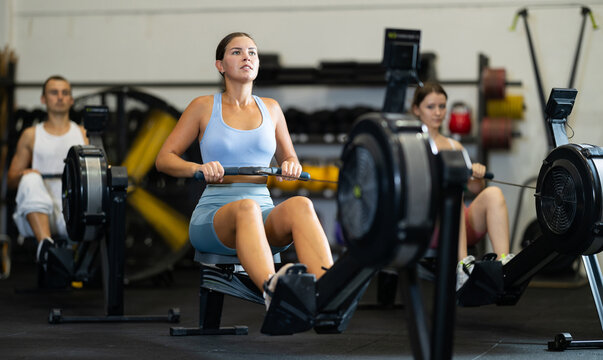 Young woman in sportswear training on rowing machine in gym
