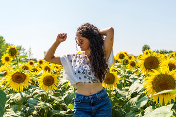 portrait of beautiful young woman with long curly hair posing in a sunflower field
