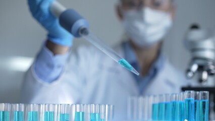 Woman scientist researcher using a micropipette to fill up test tubes with a blue liquid in...