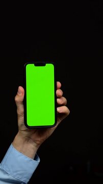Smartphone mockup with green blank screen on black isolated background in male hand.
Green display on mobile phone close-up.
Chromakey and background replacement