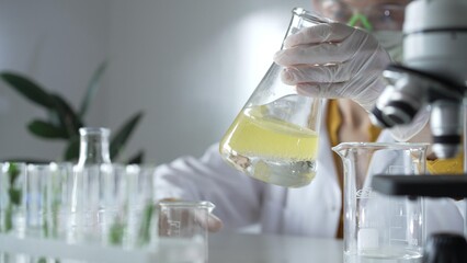 A scientist wearing white protective gloves is shaking up a yellow chemical solution inside an...