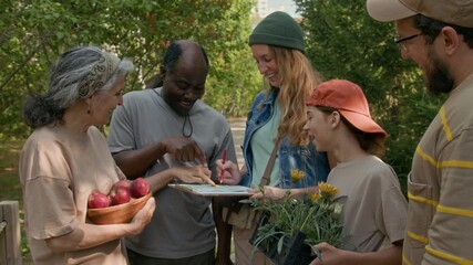 Medium shot of diverse group of activists standing in local park, holding plant pugs, studying map and discussing placement of flower beds, while decorating community garden together - Powered by Adobe