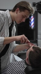 Professional barber trimming customer's hair with electric clipper, focusing on precise nape...