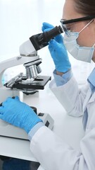 Female scientist wearing blue protective gear analyzing test samples under microscope in laboratory...
