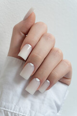 Chic white nails – feminine hand with glossy manicure in white tone, elegant beauty photo. The fingers are slightly curled, and the hand rests gently against a textured white background. 