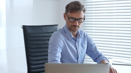 Professional accountant wearing blue sleek shirt and black glasses is concentrating while working...