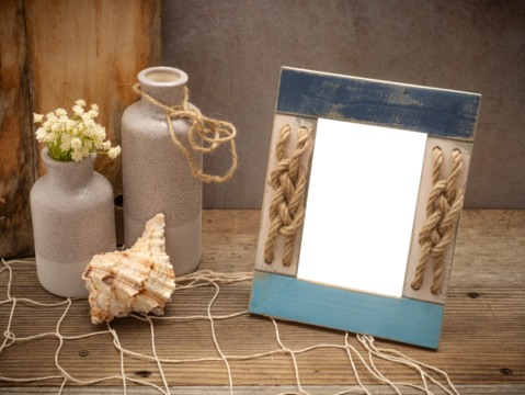 Beach coastal image with transparent picture photo frame painted blue and rope knots on a rustic old wood table, fishing fishnet netting, shells, ocean sea themed decorations. Customize DIY