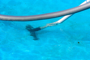 Close-up of a pool vacuum hose and cleaning head underwater in a bright blue swimming pool,...