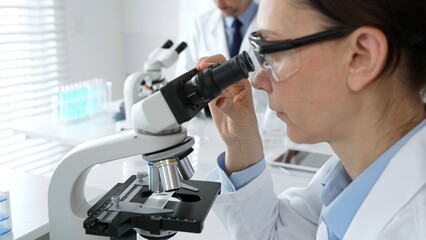 Female scientist examining specimen under microscope, conducting research in sterile laboratory...