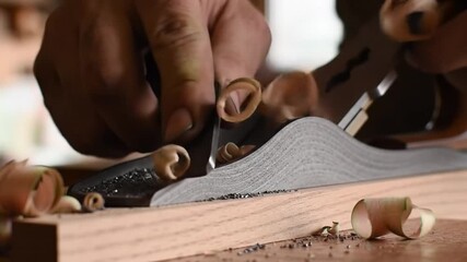 Craftsman at Work: A skilled hand meticulously planes a wooden surface with precision, revealing intricate wood shavings, evoking a sense of artisan skill and woodworking craftsmanship.