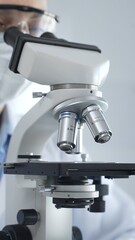 Scientist wearing lab coat and protective glasses using a modern microscope in a laboratory...