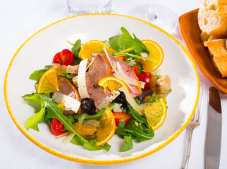 Colorful salad from duck fillets with fresh arugula, tomatoes, fried onions, sliced parmesan cheese, prunes and orange..