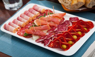 Traditional Spanish meat platter - sliced dry-cured jamon, bacon and sausages on white serving plate with olives and greens