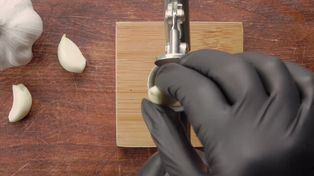 Top view of a hand placing a garlic clove into a garlic press, preparing to crush it for cooking. Close-up kitchen scene with focus on hand and utensil