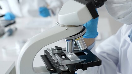 Scientific professional wearing blue protective gear examining microscope lens, performing detailed...