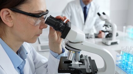 Female scientist examining specimen under microscope, conducting research in sterile laboratory...