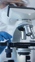 Close up of medical virologist in a hazmat suit, mask, and gloves, diligently working at a microscope in a laboratory researching viruses. Medicine and science concept