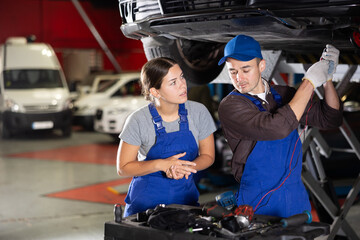 Skilled male auto-mechanic measuring capacity of automobile detail while female worker looking at...