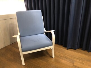 Blue armchair sits on a wood floor against a blue curtain