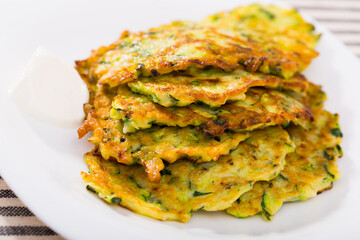 Image of zucchini fritters and white sauce at plate, top view