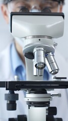 Scientist wearing lab coat and protective glasses using a modern microscope in a laboratory...
