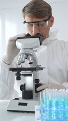 Male virologist in medical gown and gloves examines virus samples under microscope while conducting...